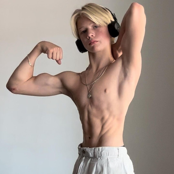 Young blond boy without a shirt flexes his muscles.