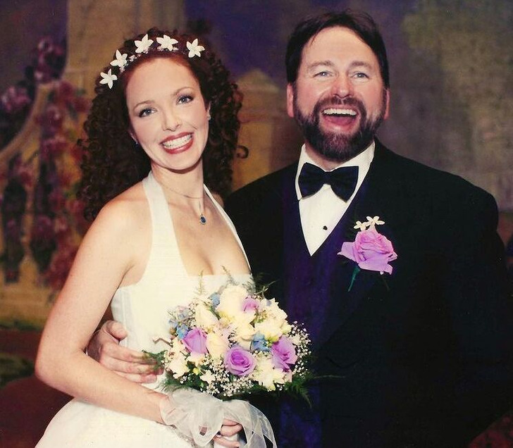 John Ritter in a black suit and tie with a curly haired woman in a white dress holding flowers.