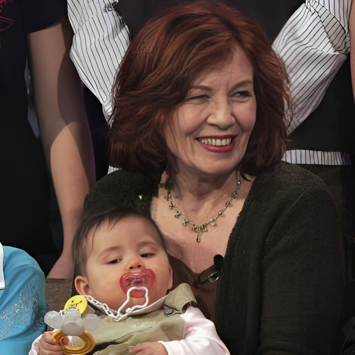 A red-haired middle-aged woman smiles with a baby holding a pacifier.
